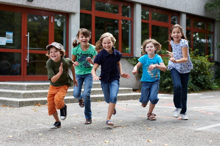 Einr Gruppe Jungen und Mädchen im Grundschulalter läuft über einen Schulhof. 
